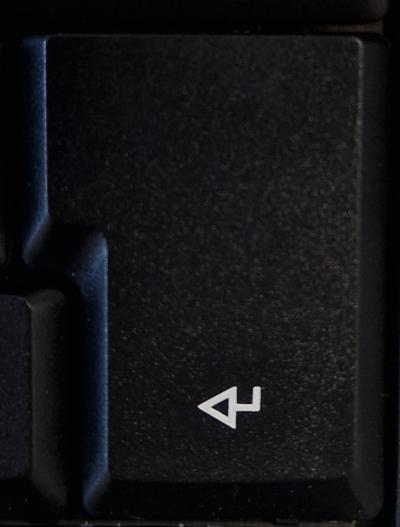 Die Enter-Taste auf einer schwarzen Computer-Tastatur: geknickter weißer Pfeil zeigt nach links