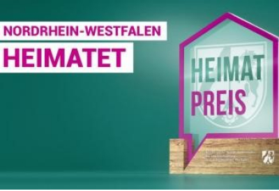 Dunkel Türkiser Hintergrund, links zwei weiße Balken mit lila Schrift "Nordrhein-Westfalen", "Heimatet", rechts lila Rahmen in Form eines Hauses mit Spitze unten links, im Rahmen hell türkis mit Wappen von NRW als Wasserzeichen, im Vordergrund oben in türkis "Heimat", darunter "Preis" in lila Schrift, unter Rahmen Balken in Holzoptik mit den Namen des Ministeriums und des Wappen von NRW