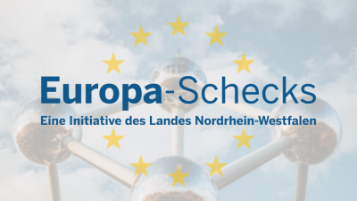Schriftzug in blau "Europa-Schecks" mittig, darunter Schriftzug in blau "Eine Initiative des Landes Nordrhein-Westfalen", Schrift umgeben von 10 gelben Sternen in Kreisform, jeweils fünf über und unter der Schrift, im Hintergrund verblasst Metallkugeln verbunden durch Metallstangen in Würfelform, Spiegelung in den Kugeln sichtbar, dahinter blauer Himmel mit weißen Wolken