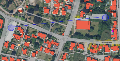 Satellit Aufnahme des Ortsteiles Brüggen: orange Formen zeigen Gebäude mit schwarzen Hausnummern, graue Straßen und Grünflächen, Straßennamen und Flurstücknummern in schwarz auf dazugehörigen Flächen, links und rechts je eine hell markierte Stelle, darauf je ein blauer Kreis verbunden durch blaue Linie zeigen alten und neuen Containerstandort, im Hintergrund mittig in gelber Schrift „32303_568, 15.06.2022“ und unten rechts „vDOP“ 