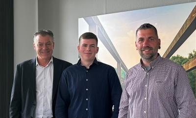 Drei Männer (von links nach rechts): Mann mit dunklem Sacko und weißem Hemd, junger Mann mit dunklen Haaren und dunkelblauen Hemd, Mann mit Bart und karriertem Hemd im Hintergrund grau Wand mit Bild von einer Brücke