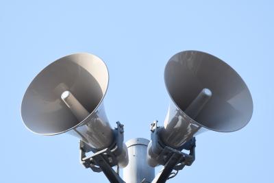 untere Frontansicht auf zwei graue Lautsprecher ausgerichtet nach links und rechts, befestigt oben an einem Mast, hellblauer Hintergrund