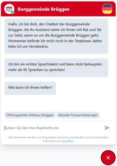 Ein Fenster mit roten Balken oben mit der Aufschrift Burggemeinde Brüggen ist zu sehen. Im Fenster ist auch das Logo der Gemeinde zu sehen. Im Dialogfenster sind dann drei Anfangsnachrichten abgebildet. Darunter befindet sich dann ein Feld, in dem man selber die Fragen formulieren und an den Chatbot stellen kann.