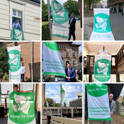 Eine Collage aus neun Bildern ist zu sehen. In jedem der Bilder stehen die Bürgermeister aus unterschiedlichen Kommunen im Kreis Viersen vor der Flagge der Mayors of Peace. Die Flagge ist grün und weiß und hat neben dem Schriftzug einen weißen Vogel abgebildet. Das mittlere Bild in der untersten Reihe zeigt Frank Gellen, Bürgermeister der Burggemeinde Brüggen, wie er vor dem Fahnenmast am Rathaus steht.