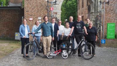 Eine Gruppe aus 10 Menschen steht vordem Eingang des Burgwalls. Vor den Leuten stehen 2 schwarze Fahrräder und ein kleines rotes Kinderfahrrad. Im Vordergrund ist das Kopfsteinpflaster und im Hintergrund grüne Pflanzen zu sehen.