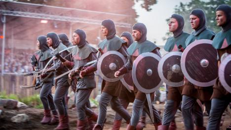 Reihe von Rittern marschiert mit Schildern und Armbrüsten nach links vor Tribüne mit Zuschauern