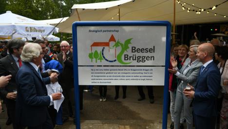 Schild mit Logo zur Städtepartnerschaft Beesel-Brüggen umgeben vom feiernden Menschen