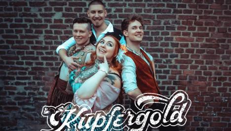 Eine vierköpfige Gruppe steht vor einer Backsteinwand. Im Vordergrund steht eine rothaarige Frau zusammen mit einem bunten rosa und blau farbigen Kleid. Im Hintergrund stehen drei Männer, die jeweils in dunklen und roten Farben gekleidet sind. Mittig unten im Bild ist der Schriftzug der Band eingeblendet.