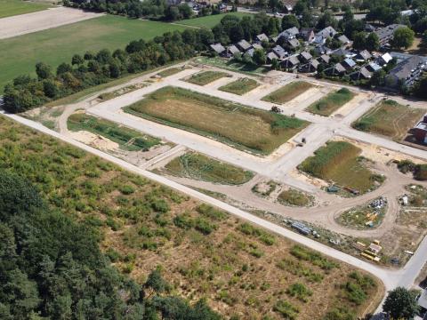 Luftbild vom Baugebiet Eichenweg mit asphaltierter Straße, sandigem und grün bewachsenen Boden, oberer und rechter Teil mit Häusern und dichtem Baumbewuchs, unterer und linker Teil des Bildes Feldlandschaft, dichter Baum- und Strauchbewuchs