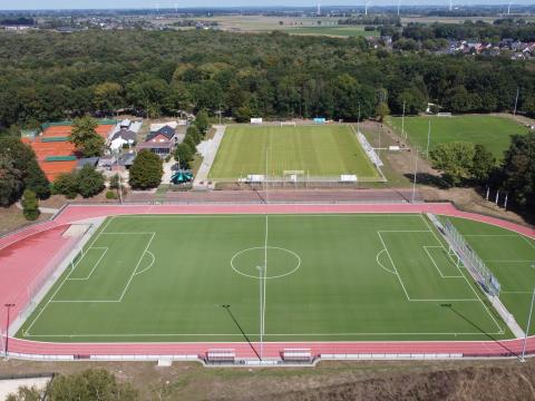 Luftbild Sportanlage Am Vennberg, im Vordergrund Kunstrasenplatz mit Laufbahn und Strahlern, im Hintergrund zwei Fußballrasenplätze, Vereinsheim, Tennisplatz, niedrige Waldzonen, Feld- und Gebäudelandschaft