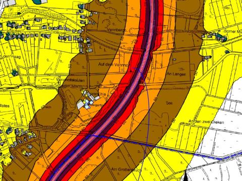Kartenauszug mit farbig markierten Bereichen für Straßenverkehrslärm, Linie für Straße von oben nach unten in pink, links und rechts davon schmaler lila Bereich, rechts und links davon roter Bereich, links und rechts davon breiterer oranger Bereich, links und rechts davon breiter brauner Bereich, links und rechts davon sehr breiter gelber Bereich, links und rechts davon weißer Bereich, Beschriftungen und Linien zum Ausweisen der Grundstücke und weiteren Anlagen in schwarz, graue Formen für Gebäude