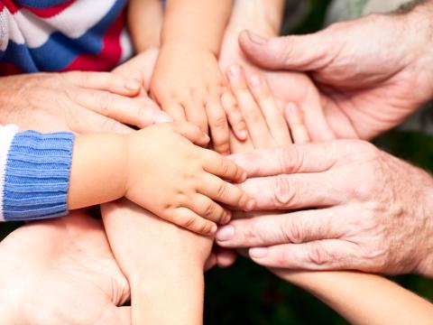 Hände verschiedener Größen und Altersstufen übereinander gelegt als Zeichen des Zusammenhaltes