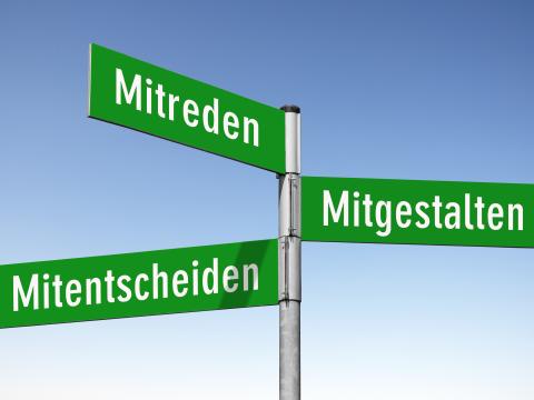 Richtungsschild mit grünen Schildern Mitreden, Mitgestalten, Mitentscheiden auf blauen Hintergrund