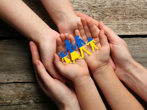 Eltern und Kind halten in ihren Händen der Größe nach auf einem Holztisch einen Papierfamilienausschnitt in den Farben der ukrainischen Flagge