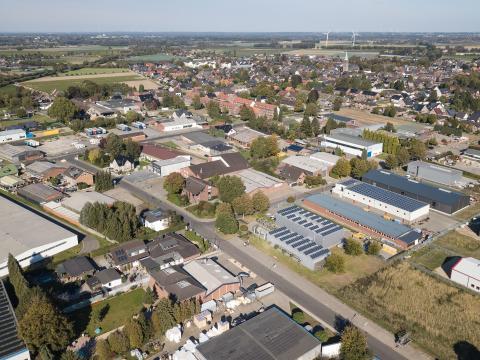 Panoramablick über Gewerbegebiet Brüggen mit Straßen, Bäumen, verschiedenen Grünflächen und Gebäuden, im Hintergrund Feld-, Gebäude- und Waldlandschaft bei grau, bewölktem Himmel